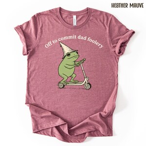 Puede incluir: Camiseta color malva jaspeado con un dibujo de una rana en un patinete, con un sombrero de mago. El texto "Off to commit dad foolery" est&aacute; sobre la rana. La camiseta es de material suave.