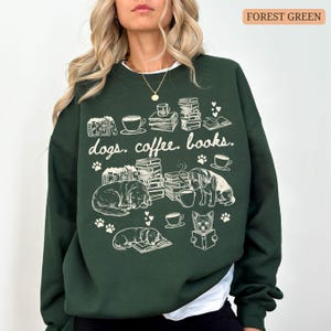 May include: Forest green sweatshirt with the words "dogs. coffee. books." and illustrations of dogs, books, and coffee cups. The design is in white. The sweatshirt has a white collar.