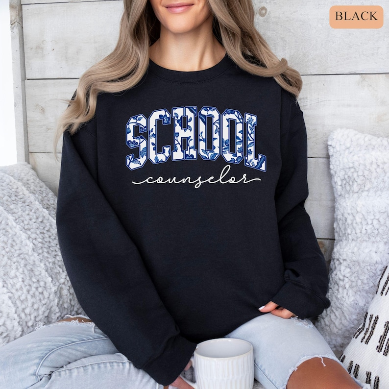 May include: Black sweatshirt with the word "SCHOOL" in large, blue floral print letters, and the word "counselor" in cursive below. The sweatshirt is a crew neck style.