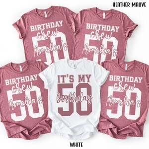 May include: Four heather mauve t-shirts and one white t-shirt. The mauve shirts feature white text reading BIRTHDAY crew, Amelia's, and a large 50. The white shirt features mauve text reading IT'S MY 50 birthday. Text HEATHER MAUVE and WHITE is visible.