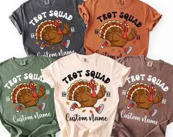 May include: Five short-sleeved t-shirts in various colors, including gray, orange, green, ivory, and brown. Each shirt features a cartoon turkey wearing sneakers and the text "TROT SQUAD" with the option for a custom name.