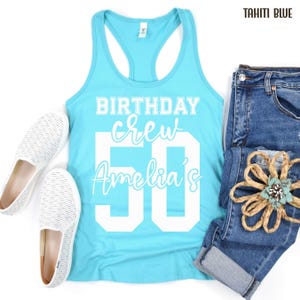 May include: A Tahiti blue racerback tank top with white text that reads BIRTHDAY crew Amelia's 50, paired with blue denim jeans and white slip-on shoes with a fine horizontal stripe pattern and a decorative tan rope flower accessory.