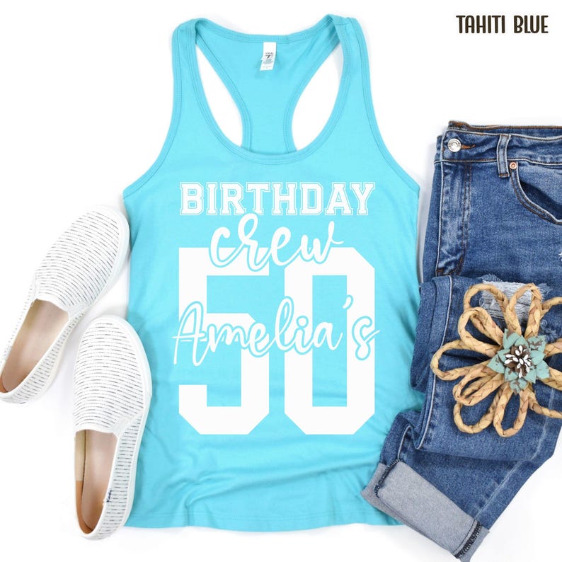 May include: A Tahiti blue racerback tank top with white text that reads BIRTHDAY crew Amelia's 50, paired with blue denim jeans and white slip-on shoes with a fine horizontal stripe pattern and a decorative tan rope flower accessory.