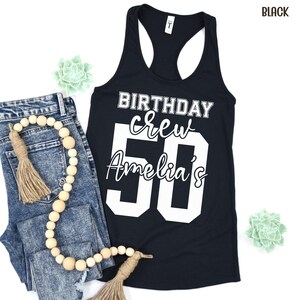 May include: A black racerback tank top featuring white screen-printed text that reads BIRTHDAY crew Amelia's 50. The design uses a combination of bold block lettering and a cursive script font to display the birthday celebration message clearly.