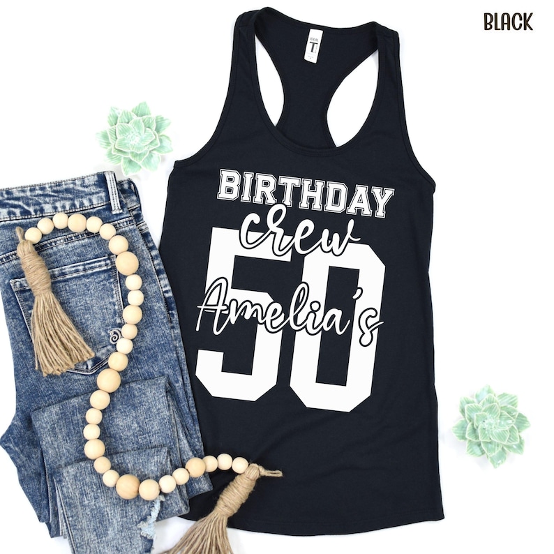 May include: A black racerback tank top featuring white screen-printed text that reads BIRTHDAY crew Amelia's 50. The design uses a combination of bold block lettering and a cursive script font to display the birthday celebration message clearly.