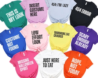 May include: A collection of colorful t-shirts with humorous phrases printed on them. The shirts are in various colors, including green, pink, blue, and yellow, with phrases like "This is my look" and "Just here to eat."