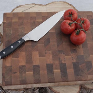 Peut inclure: Une planche à découper en bois avec un couteau de chef en acier inoxydable et un groupe de tomates rouges. La planche est faite de différentes nuances de bois et repose sur une souche d'arbre.
