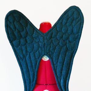 May include: A pair of dark blue felt wings with a quilted design, displayed on a red dress form.