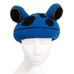 May include: Blue fleece frog hat with black spots and ears. The hat is on a white mannequin head.