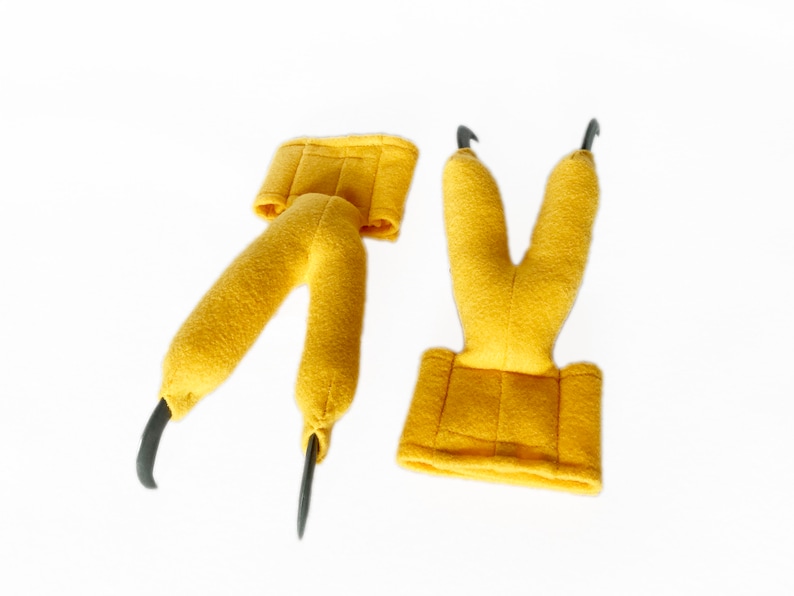 Pode incluir: Dois fantoches de m&atilde;o de feltro amarelo com garras pretas. Os fantoches s&atilde;o projetados para parecer p&eacute;s de p&aacute;ssaro.