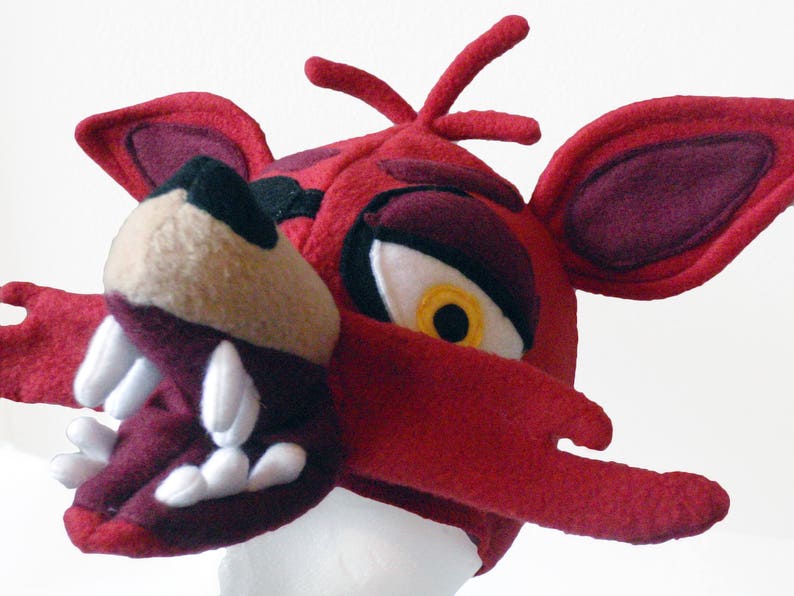 Puede incluir: Disfraz de cabeza de zorro de felpa roja con un ojo blanco y amarillo, dientes afilados y una nariz burdeos.