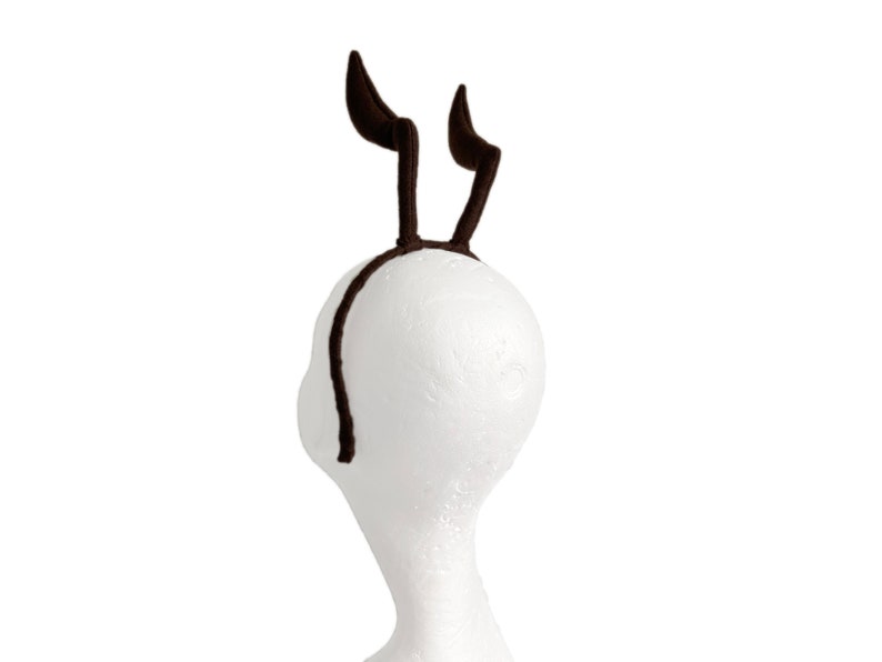 May include: A brown headband with two brown fuzzy antlers attached to it.