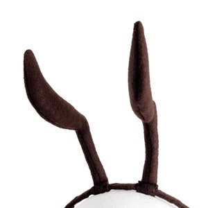 May include: A pair of brown felt bunny ears headband. The headband is made of a soft, brown felt material. The ears are long and pointed, and they are attached to a headband that is made of a white elastic material.