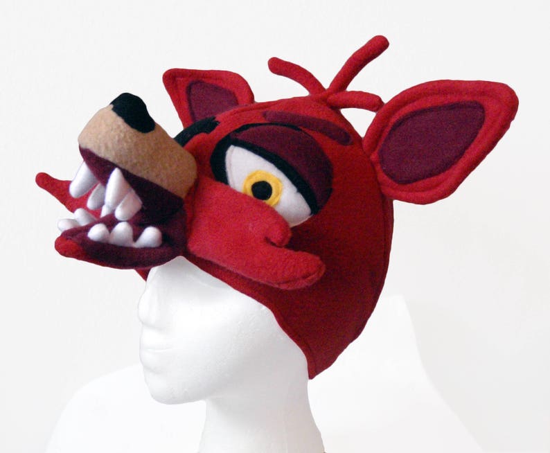 Puede incluir: Disfraz de cabeza de Foxy el Zorro Pirata de felpa roja con dientes blancos y un ojo amarillo. El disfraz se lleva en una cabeza de maniqu&iacute; blanca.