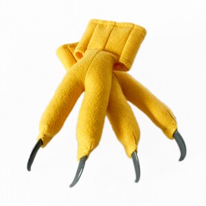 Pode incluir: Marioneta de m&atilde;o de feltro amarelo com tr&ecirc;s garras. As garras s&atilde;o de pl&aacute;stico cinza.