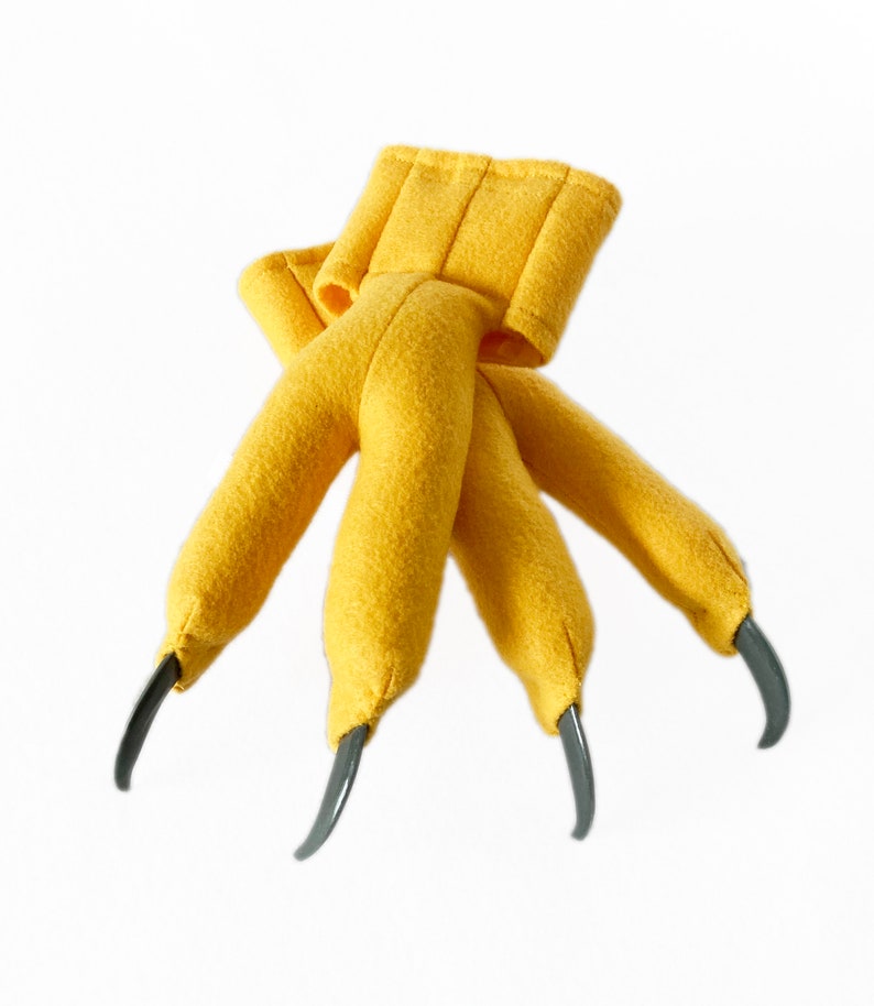 Pode incluir: Marioneta de m&atilde;o de feltro amarelo com tr&ecirc;s garras. As garras s&atilde;o de pl&aacute;stico cinza.