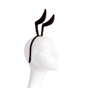 May include: A pair of brown bunny ears headband with a black headband.