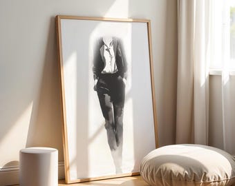 May include: A framed black and white print of a person in a suit, leaning against a wall. The artwork is in a light wood frame. A white cylindrical stool and a round, beige floor cushion are in the foreground.