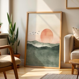 Op de afbeelding: Een ingelijste kunstafdruk met een zonsondergang boven groene heuvels. Het kunstwerk toont een oranje zon, silhouetten van vogels en een zacht kleurenpalet. Het frame is gemaakt van lichtgekleurd hout.