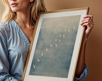 May include: A framed art print featuring a flock of white birds in flight against a soft blue and gray background. The artwork is encased in a gold-colored frame with a white matting, creating a classic and elegant aesthetic.