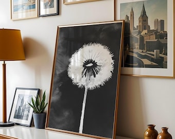 May include: A large framed print featuring a black and white dandelion illustration. The artwork has a gold frame and is leaning against a white wall. Other framed art pieces and a lamp are also visible.