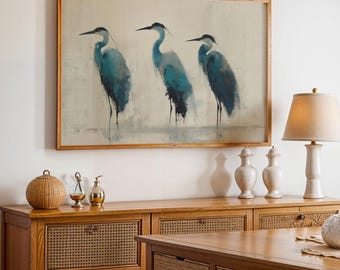 May include: A framed print depicting three blue herons in a minimalist style. The birds are painted in shades of blue and black against a neutral backdrop. The artwork hangs above a wooden cabinet with woven detailing.