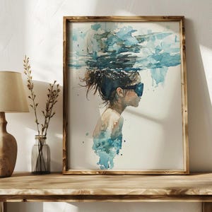 Può includere: Stampa ad acquerello di una persona sott'acqua, con occhialini. L'opera presenta sfumature di blu e bianco, con una cornice in legno. I capelli della persona sono raccolti e l'immagine cattura la sensazione di essere immersi nell'acqua.