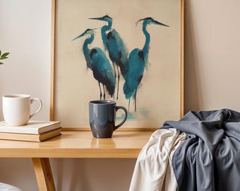 May include: A framed print of three blue herons in a watercolour style. The artwork is set against a neutral backdrop. A white mug and a dark grey mug are on a wooden surface.