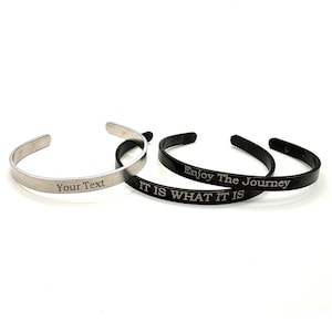 May include: Three metal cuff bracelets. One is silver with the text "Your Text". The other two are black, one with "Enjoy The Journey" and the other with "IT IS WHAT IT IS".