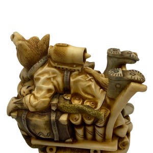 K&ouml;nnte beinhalten: Eine Keramikfigur eines Hundes, der eine Milit&auml;runiform tr&auml;gt und eine gro&szlig;e Tasche und andere Vorr&auml;te auf einem kleinen Wagen transportiert. Der Hund tr&auml;gt einen Helm und hat einen entschlossenen Gesichtsausdruck.