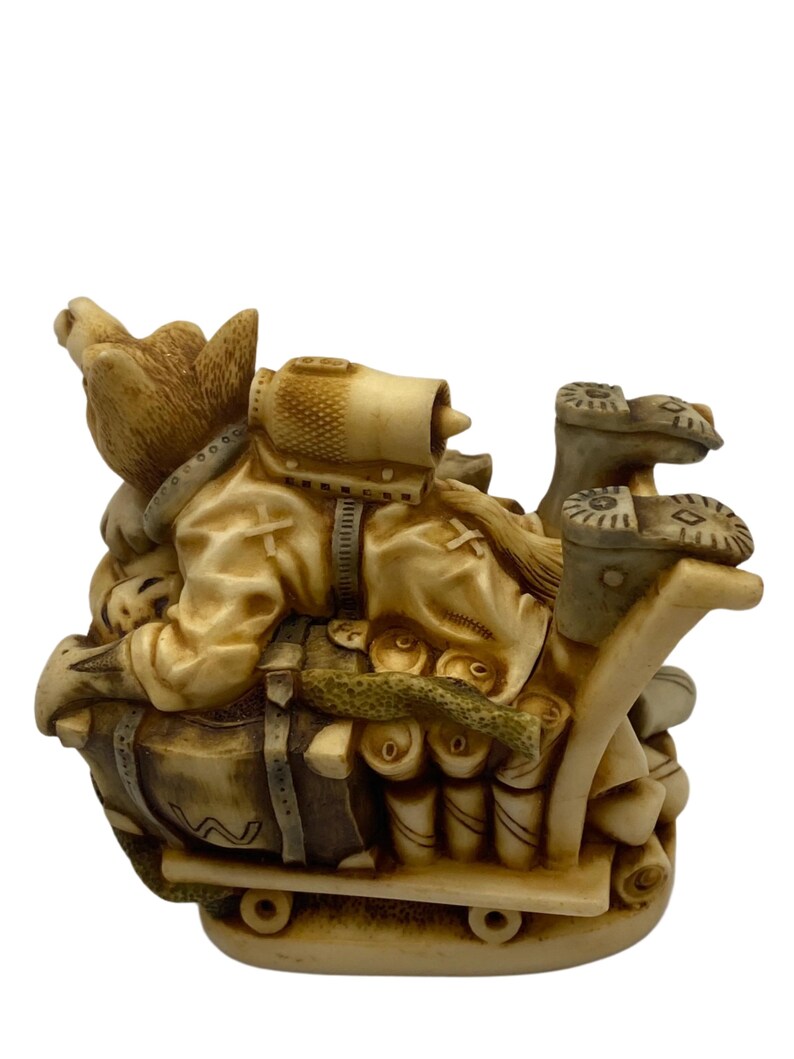K&ouml;nnte beinhalten: Eine Keramikfigur eines Hundes, der eine Milit&auml;runiform tr&auml;gt und eine gro&szlig;e Tasche und andere Vorr&auml;te auf einem kleinen Wagen transportiert. Der Hund tr&auml;gt einen Helm und hat einen entschlossenen Gesichtsausdruck.