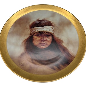 Puede incluir: Plato decorativo con borde dorado. El centro presenta un retrato de una persona con cabello largo y oscuro y una diadema blanca. La persona lleva una prenda oscura y tiene una expresión seria. La obra está firmada en la esquina inferior izquierda.