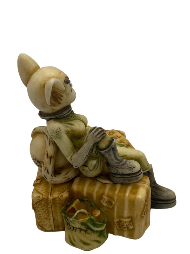 K&ouml;nnte beinhalten: Eine Keramikfigur einer Frau mit Hasenohren, die eine gr&uuml;n-braune Uniform tr&auml;gt und auf Gep&auml;ck sitzt. Das Gep&auml;ck ist mit den Worten "Space", "Plum" und "Western Isles of Scotland" beschriftet.