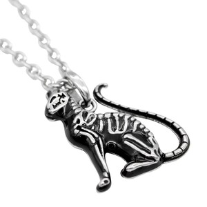 May include: A silver chain necklace with a black cat pendant. The cat is depicted as a skeleton with a detailed bone structure. The pendant is a statement piece with a gothic aesthetic.