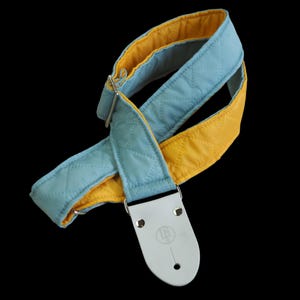 May include: A blue and yellow guitar strap with a quilted design and white leather ends.