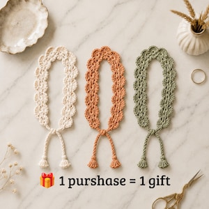 May include: Three crocheted bookmarks in cream, terracotta, and sage green, each featuring a scalloped edge design and two dangling cords with small tassels at the ends. The text "1 purshase = 1 gift" is printed below the bookmarks with a gift icon.