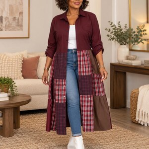 May include: A long-sleeved, button-down shirt dress featuring a solid dark burgundy top section and a lower section composed of patchwork panels in red plaid, dark burgundy, and solid brown fabric, worn over blue denim jeans and white boots.