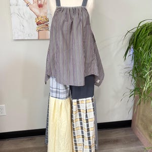 May include: A sleeveless top with thin straps featuring a dark grey and white vertical stripe pattern, paired with wide-leg trousers constructed from a patchwork of solid dark grey, light yellow, and grey-and-white plaid fabric panels.