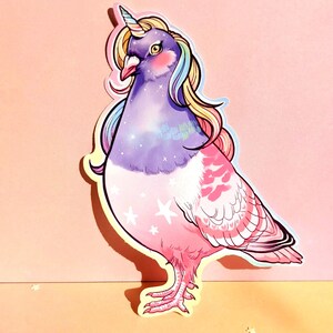 May include: A sticker featuring a whimsical illustration of a pigeon with a unicorn horn and flowing rainbow hair. The bird has a purple head and chest, transitioning to pink feathers with star accents. The background is a gradient of pink and peach.