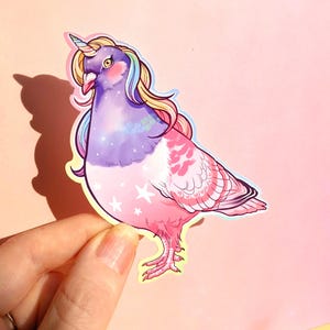 May include: A sticker featuring a whimsical illustration of a pigeon transformed into a unicorn. The bird has a purple body, pink wings, and a rainbow mane and horn. White stars decorate the lower body, and the background is a soft pink.