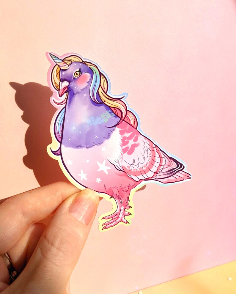May include: A sticker featuring a whimsical illustration of a pigeon transformed into a unicorn. The bird has a purple body, pink wings, and a rainbow mane and horn. White stars decorate the lower body, and the background is a soft pink.