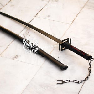 May include: A black katana sword with a red and black wrapped handle and a black chain attached to the end. The sword is lying on a white tiled surface.