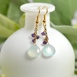 Peut inclure: Boucles d'oreilles pendantes avec crochets et chaînes en métal doré, ornées de petites perles d'améthyste violette à facettes et d'une pierre de calcédoine bleu pâle en forme de goutte lisse à la base de chaque boucle.