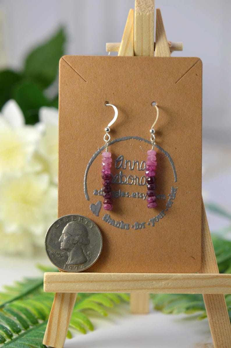 May include: Dangle earrings featuring faceted pink and deep magenta gemstone beads on silver-toned hooks. The earrings are displayed on a brown card next to a United States quarter coin for scale, showing the beads arranged in a vertical gradient.