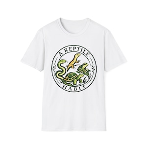 Pode incluir: Uma t-shirt branca de manga curta com um gráfico circular no peito. O design inclui uma cobra verde, um lagarto amarelo, um sapo verde e uma tartaruga verde com o texto A REPTILE HABIT escrito numa borda circular preta.