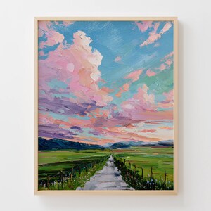 May include: An oil painting of a landscape with a road leading into the distance. The sky is filled with pink and purple clouds against a blue sky. Green fields and mountains are in the background. The painting is in a light wood frame.