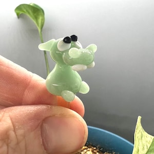 May include: A light green glass figurine of a cartoon dog with black eyes and white accents. The figurine is attached to a clear glass rod.