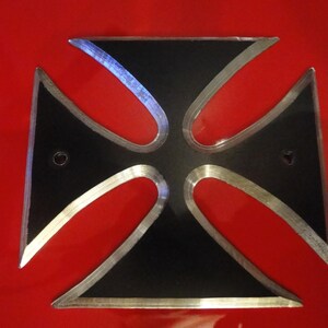 Puede incluir: Una cruz de metal negro con un borde plateado. La cruz est&aacute; sobre un fondo rojo.