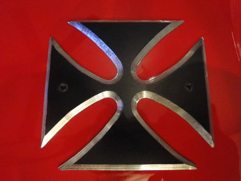 Puede incluir: Una cruz de metal negro con un borde plateado. La cruz est&aacute; sobre un fondo rojo.