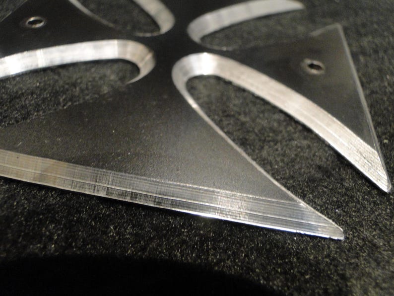 Puede incluir: Una cruz de metal plateado con un dise&ntilde;o afilado y puntiagudo. La cruz est&aacute; hecha de dos capas de metal, creando un efecto de capas.